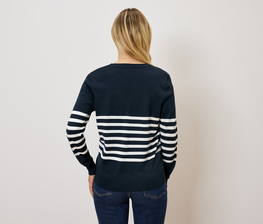 Zezadu je vidět žena s blond vlasy v modrobílém pruhovaném svetru a džínách.