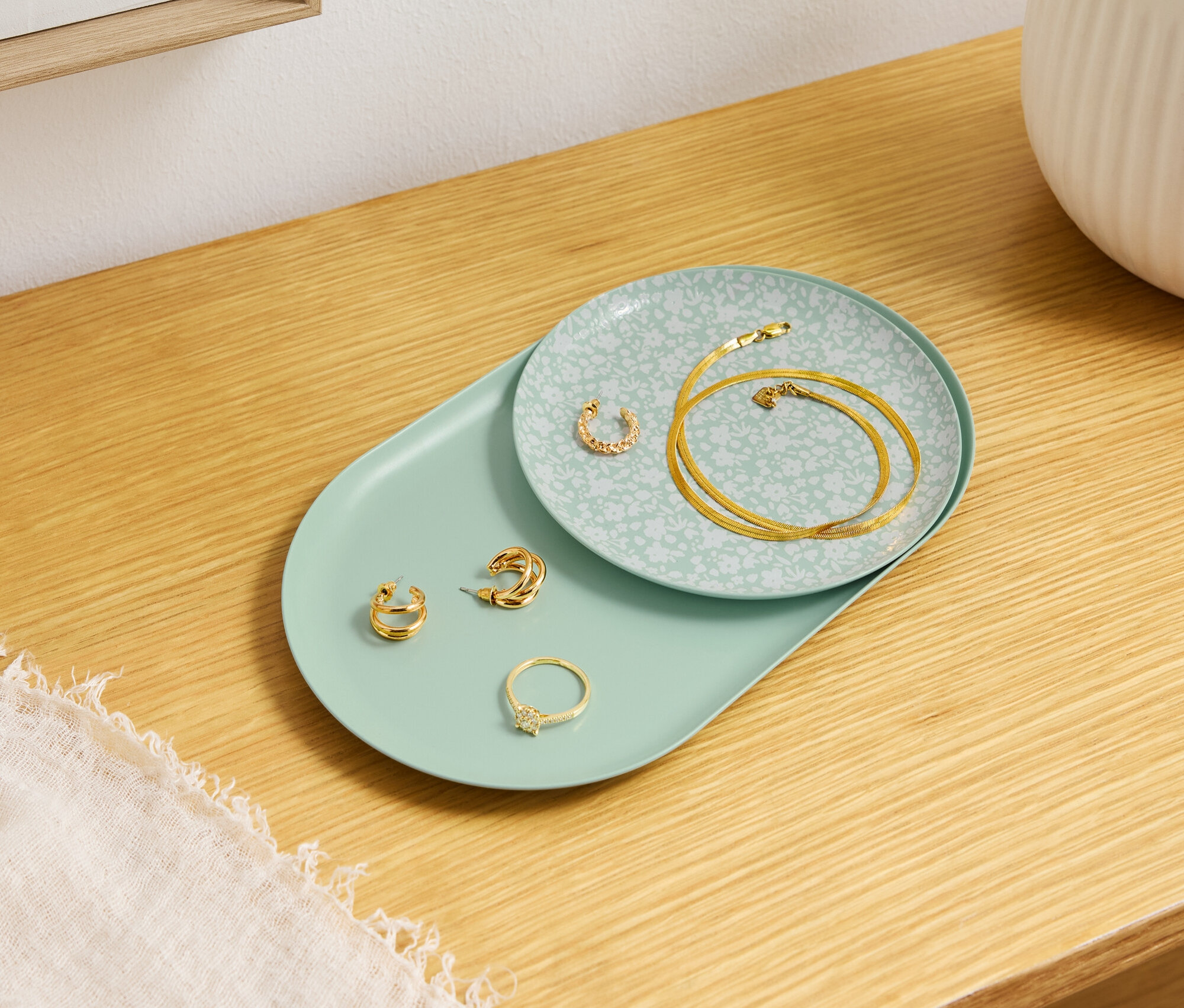 Zlaté šperky leží na ozdobných talířích na dřevěném stole.