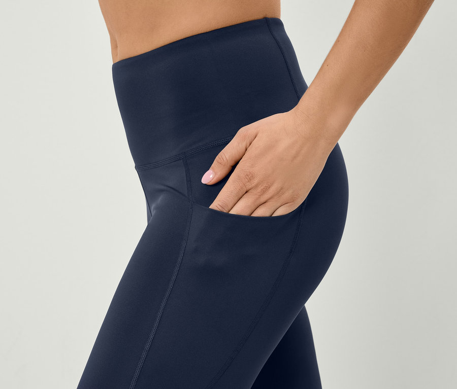 Žena dává ruku do kapsy tmavě modrých legín.