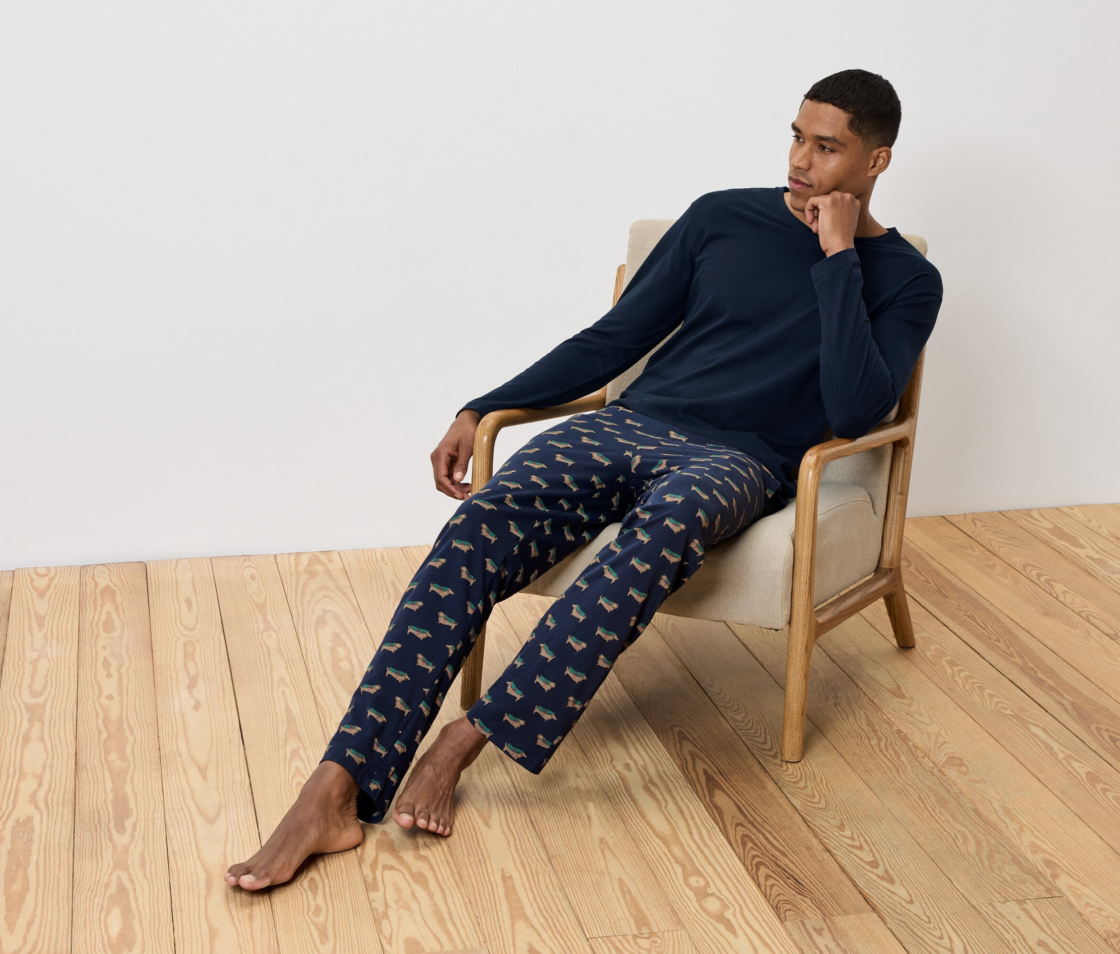 Muž sedí v křesle a má na sobě tmavě modré pyžamo s potiskem jezevčíků.