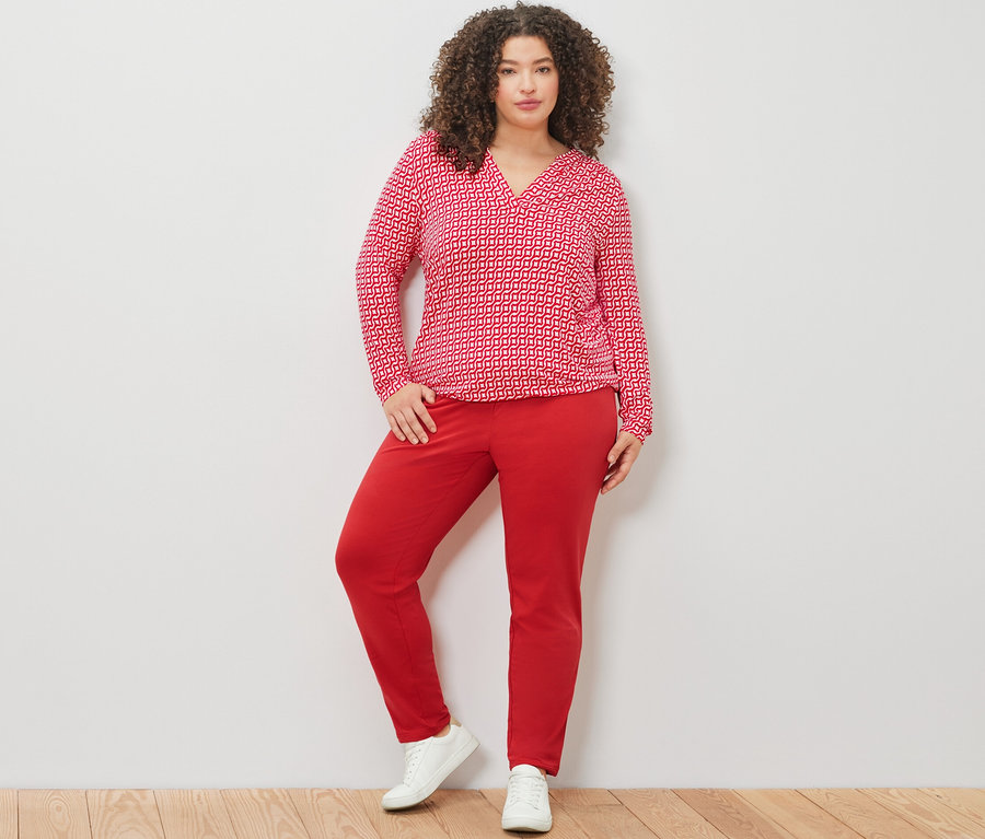 Žena pózuje v červeném halenkovém triku s potiskem a červených kalhotách joggpant.