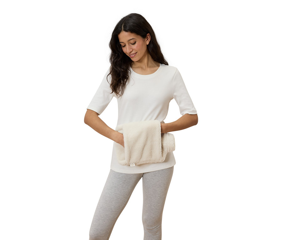 Žena drží v rukou krémově bílý hřejivý polštář.