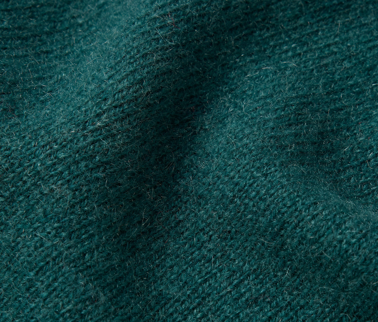 Detailní záběr na texturu tmavě zelené pleteniny.