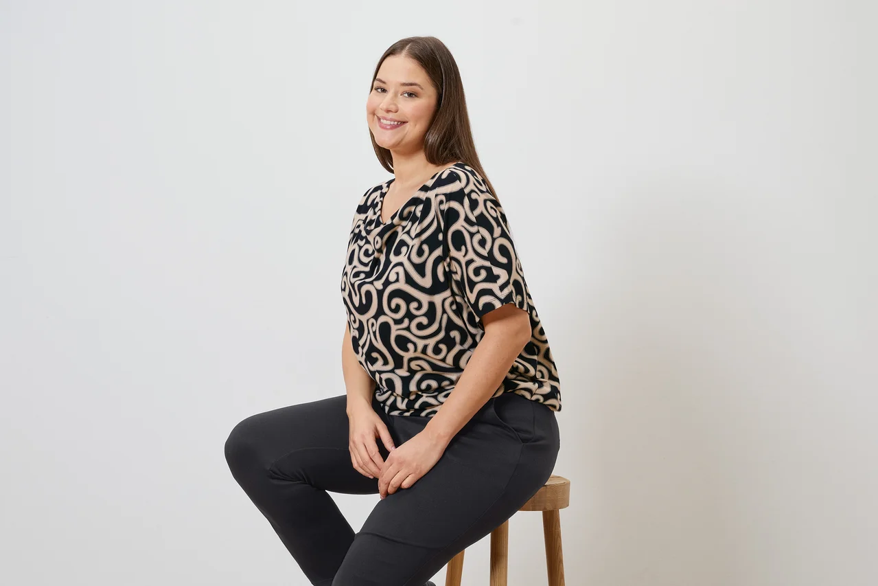 Žena sedí na stoličce a má na sobě vzorovanou blůzu a kalhoty joggpant.