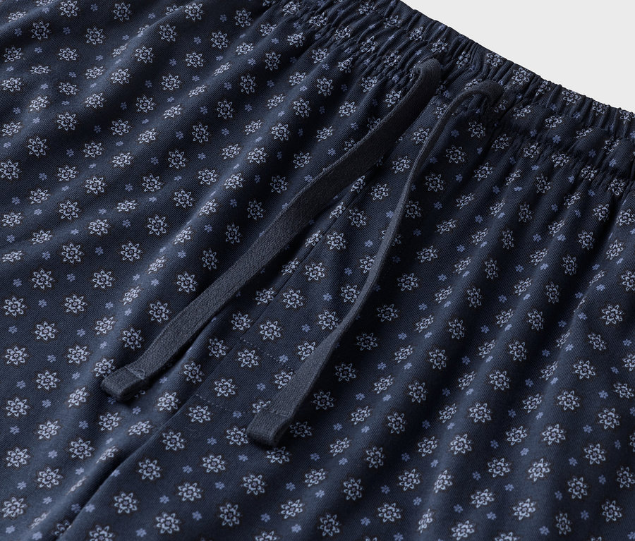 Detailní záběr na tmavě modré pyžamové kalhoty s květinovým vzorem se stahovací šňůrkou.