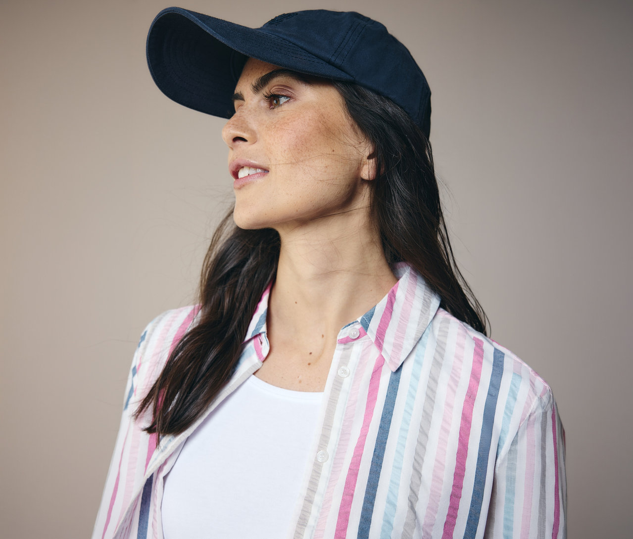 Žena v tmavě modré kšiltovce a pruhované košilové halence CECIL se dívá doleva.