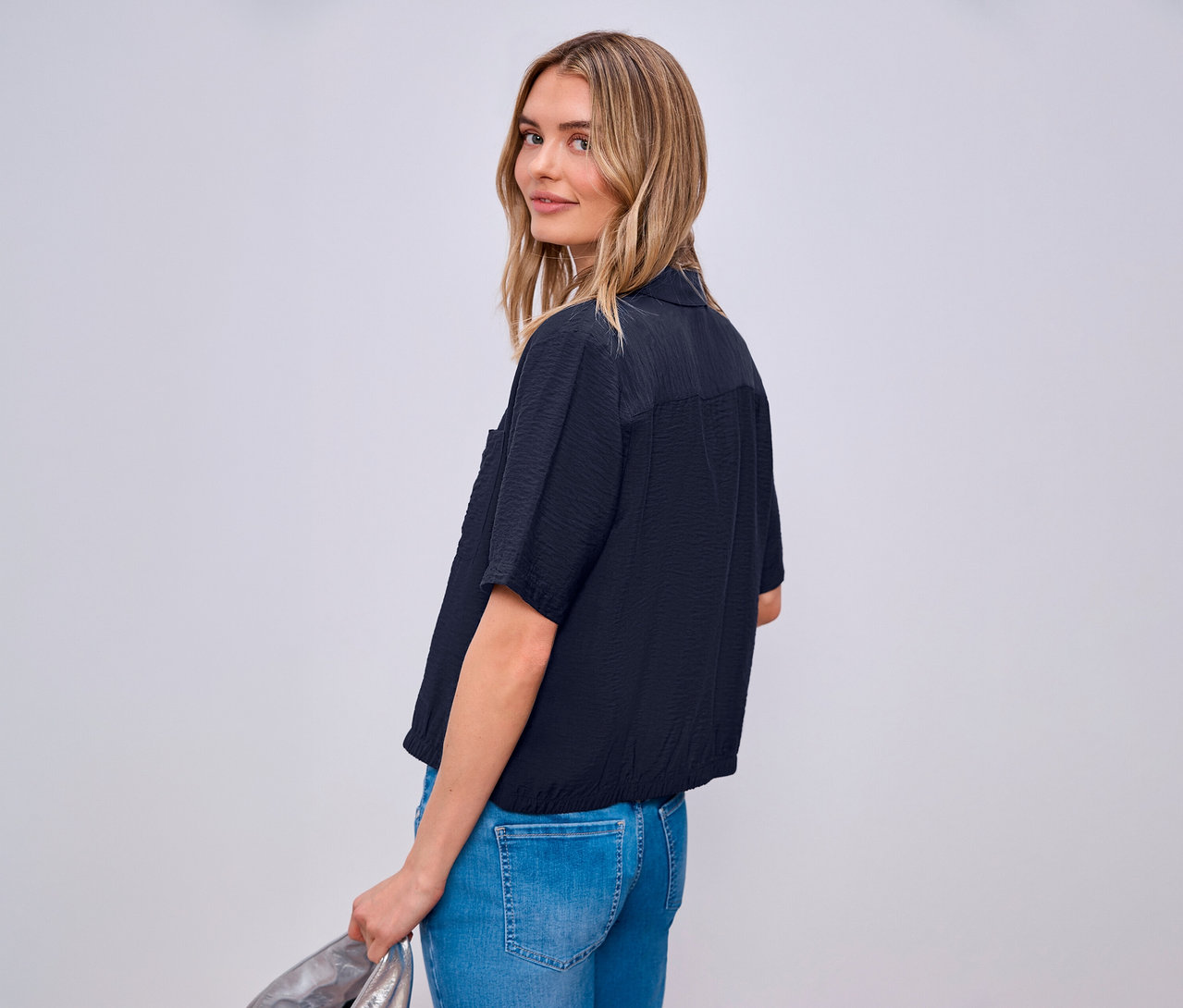 Žena se dívá přes rameno a má na sobě košilovou halenku Street One a džíny.