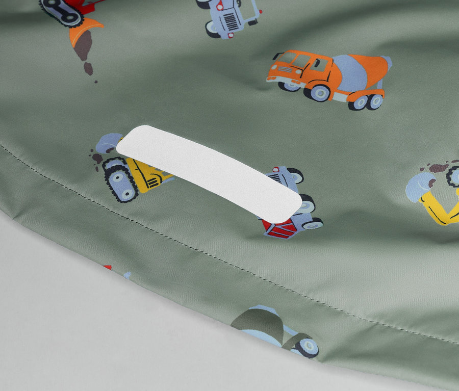 Detailní záběr olivově zelené látky s barevnými stavebními vozidly a bílou náplastí.