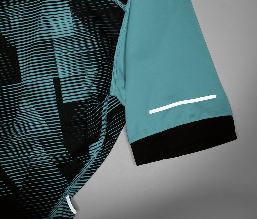 Detail cyklistického dresu s tyrkysovým rukávem, černou manžetou a reflexním pruhem.