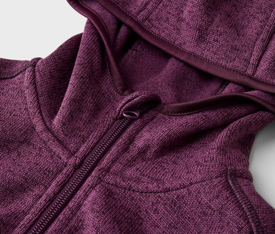 Detailní záběr na částečně rozepnutou vínovou mikinu s kapucí na zip.