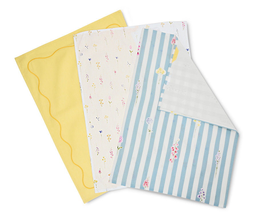 Tři utěrky leží na sobě: žlutá se zvlněným okrajem, krémová s květinovými vzory a modro-bílá pruhovaná s květinami.