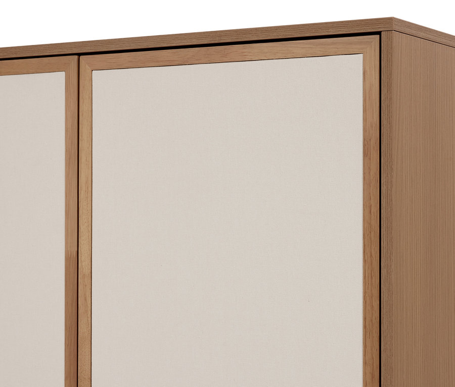 Detail světle hnědé dřevěné skříně se dvěma světle béžovými látkovými panely. Pravá strana ukazuje dřevěný boční panel skříně.