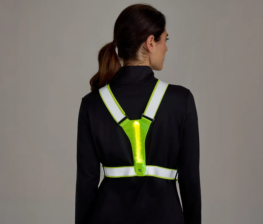 Žena zezadu v černém tričku s dlouhým rukávem a neonově žluté reflexní vestě s vertikálním světelným pruhem na zádech.