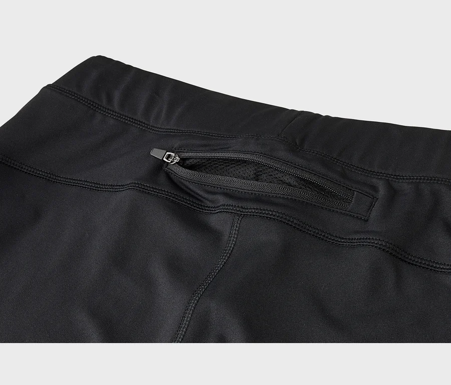 Detail černého sportovního oblečení s kapsou na zip na zadní straně, přes kterou je vidět síťovaná podšívka.