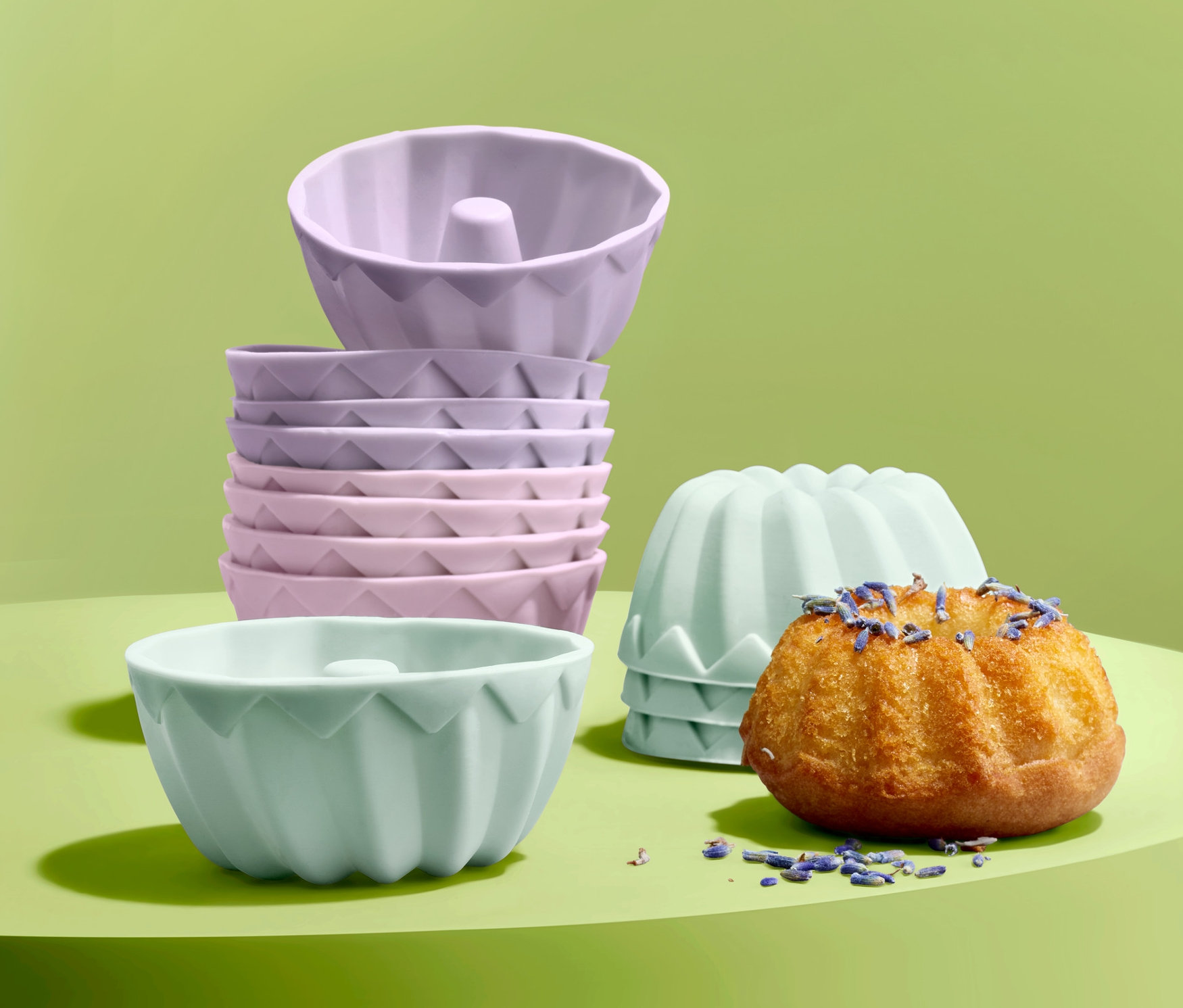 Na zeleném pozadí jsou formičky na minibábovky, 12 ks, jedna bábovka je ozdobená levandulí.