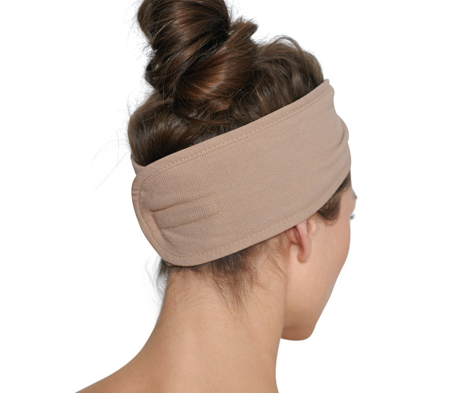 Žena s hnědými vlasy staženými do drdolu nosí kosmetickou čelenku v barvě béžové.