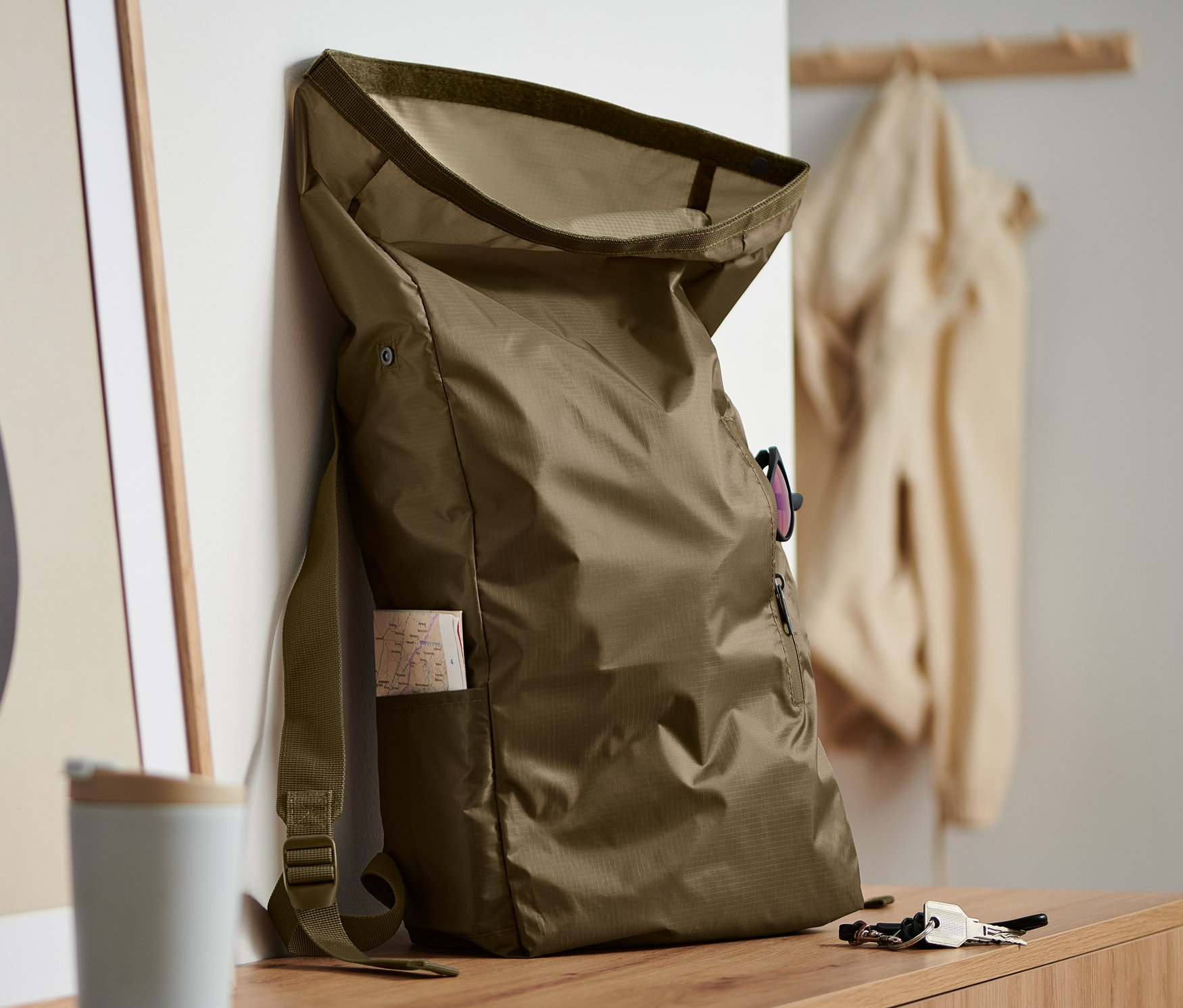 Khaki skládací batoh opřený o zeď vedle abstraktního uměleckého díla.