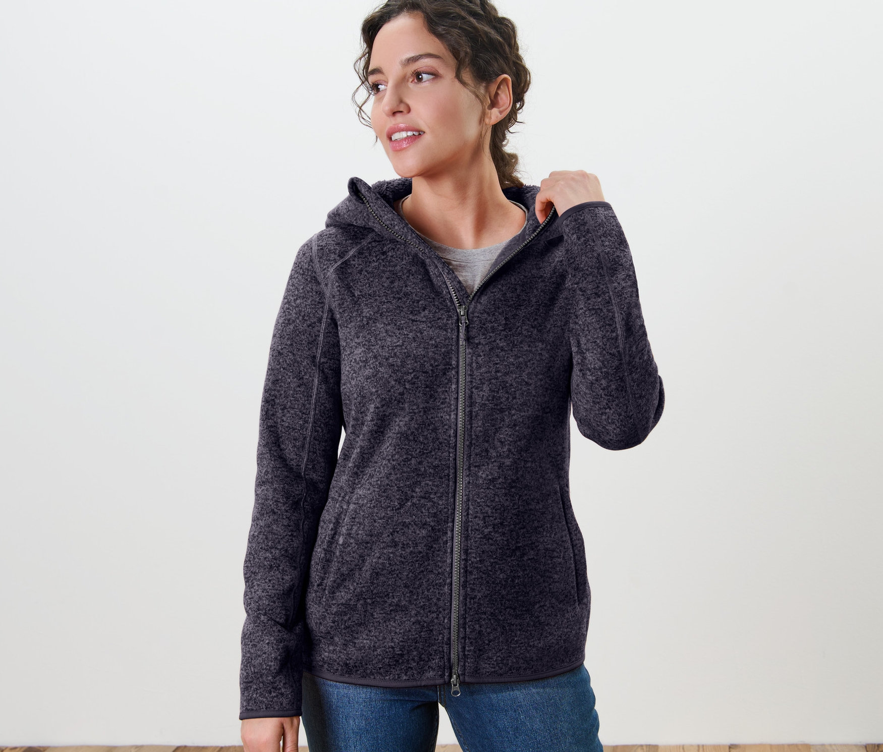 Žena má na sobě bundu z pleteného fleecu s kapucí, tmavě modrá s melírem.