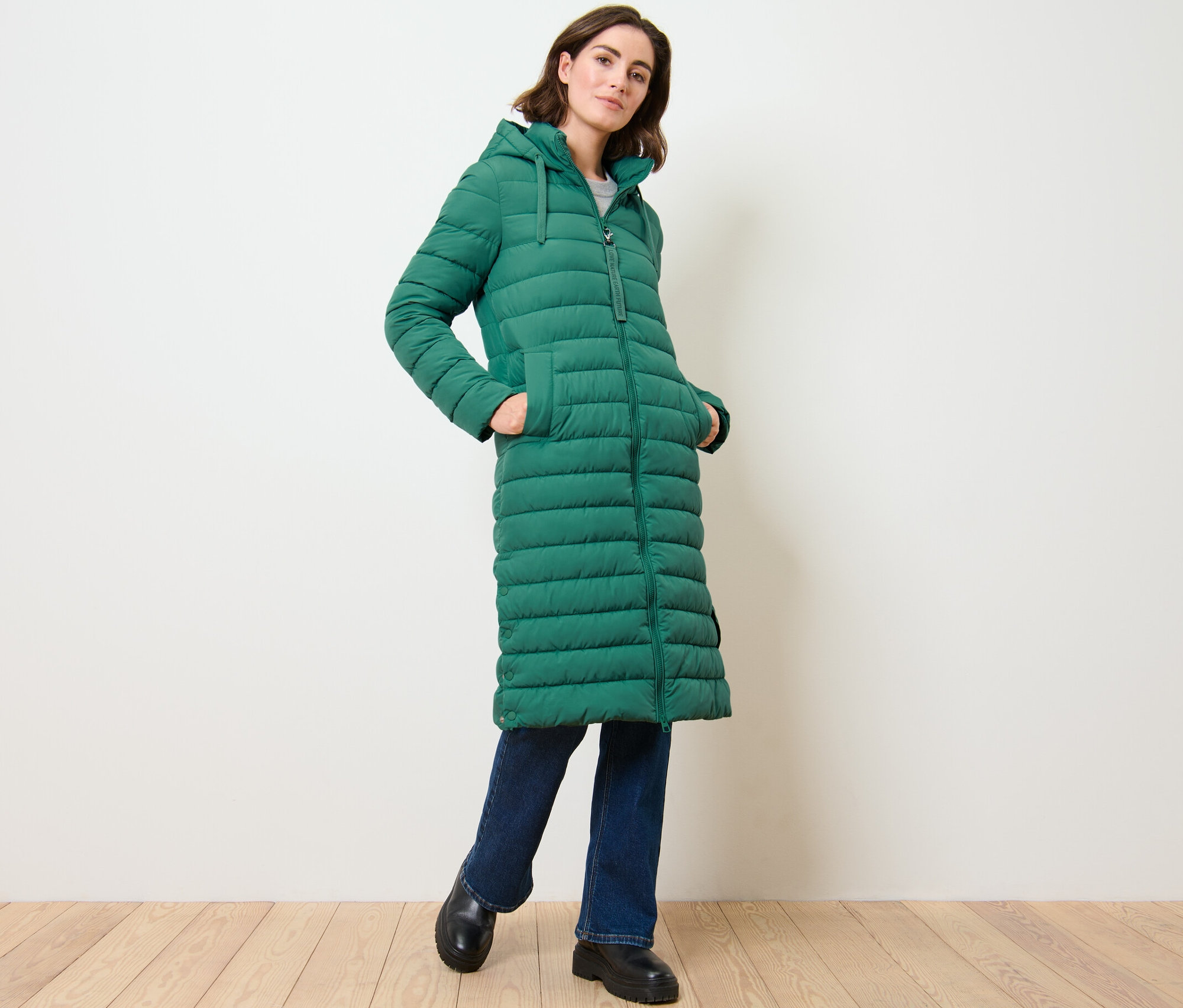 Žena pózuje v dlouhém prošívaném kabátu s kapucí.