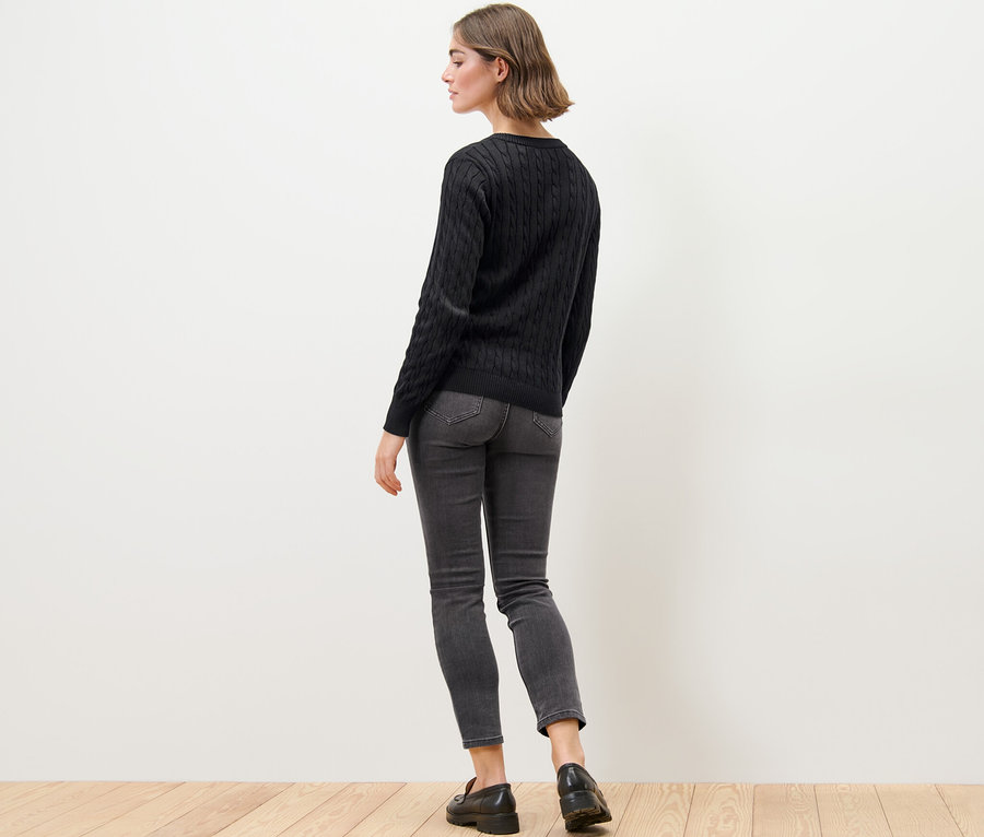 Žena má na sobě kardigan z jemného úpletu s copánkovým vzorem, džíny a mokasíny.