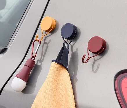 Na šedém autě jsou připevněny tři magnetické háčky. Na jednom háčku visí ručník a na druhém svítilna.