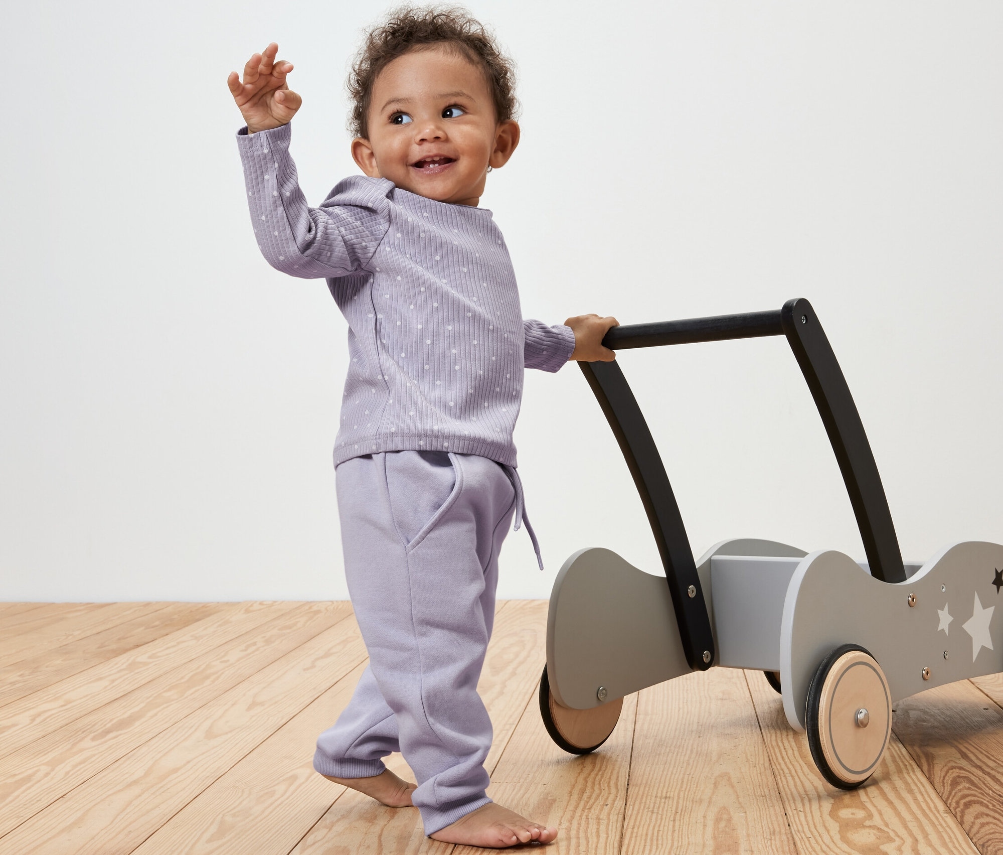 Dítě tlačí chodítko na kolečkách a má na sobě teplákové kalhoty s puntíky.