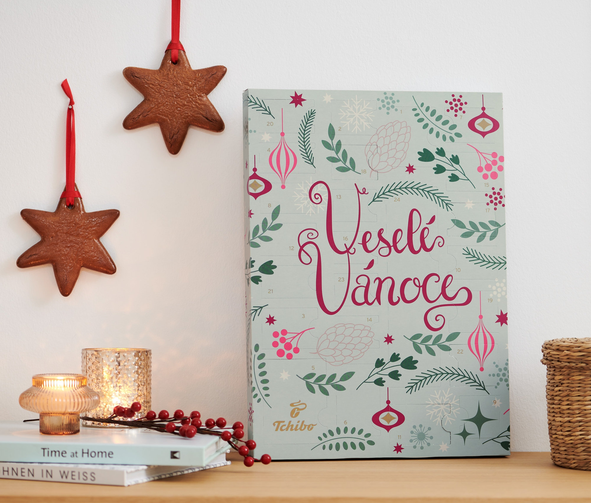 Adventní kalendář Tchibo stojí na dřevěné komodě vedle knih a dekorací.