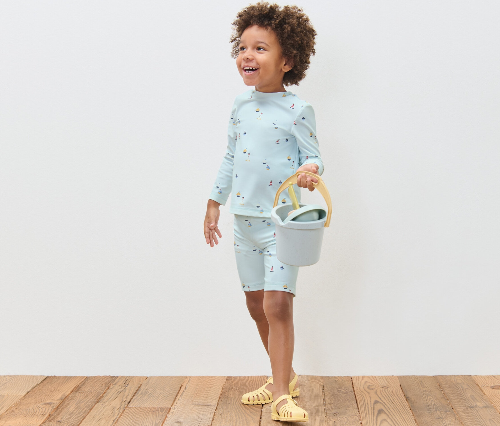 Chlapec v dětské soupravě s UV faktorem 80 s námořnickým motivem drží kyblík a lopatku.