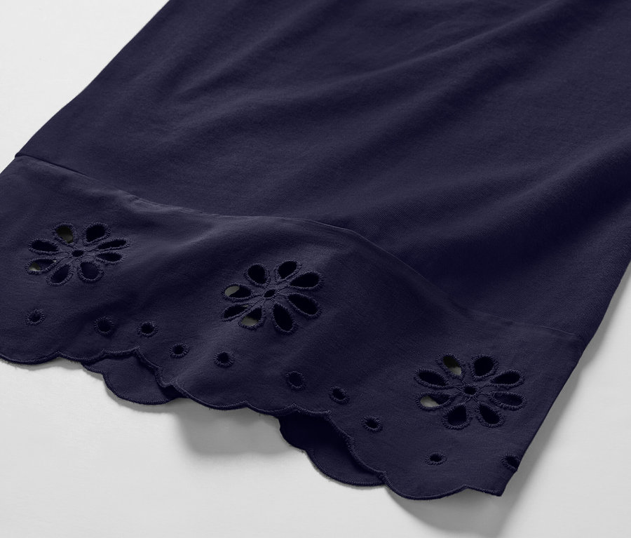 Detailní záběr na tmavě modré culottes kalhoty s výšivkou květin na lemu.