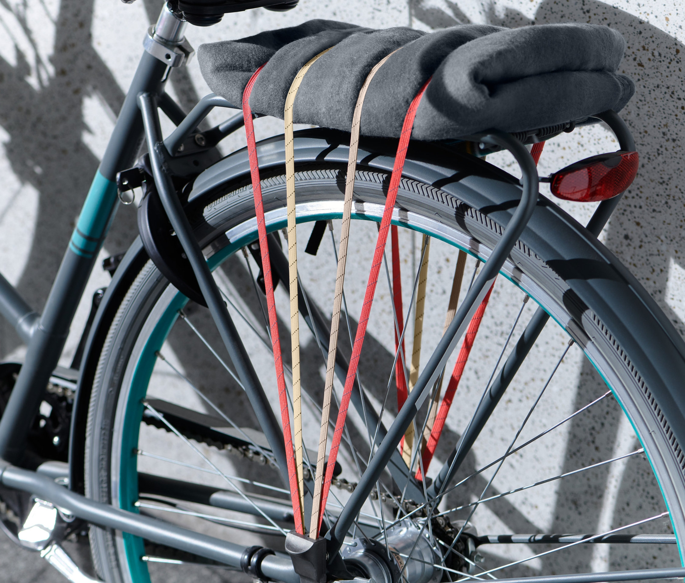 Šedá deka je připevněna k nosiči jízdního kola pomocí upínacího popruhu na jízdní kolo.