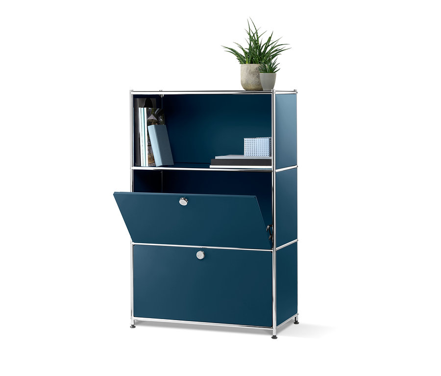 Modrá komoda »CN3« se 2 zásuvkami, jedna zásuvka je otevřená. Nahoře jsou knihy a rostlina v květináči.