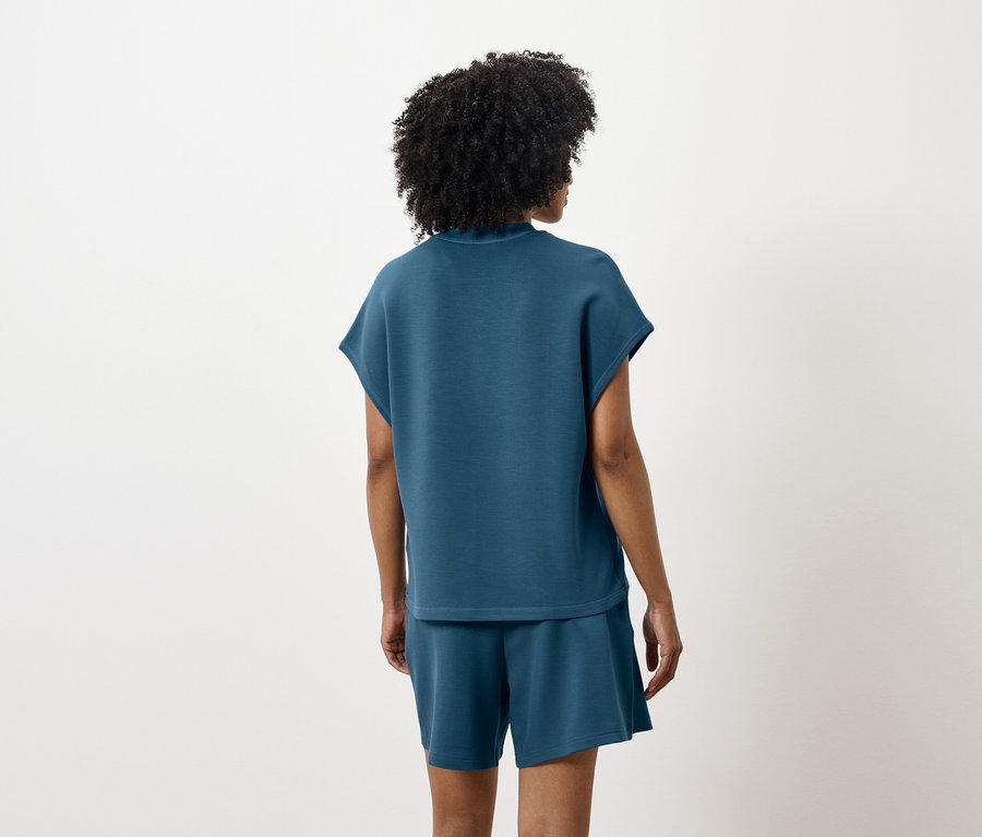 Žena stojí zády a má na sobě modrozelený top a šortky.