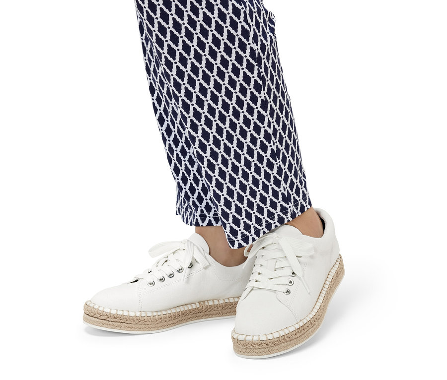 Nohy v modrobílých vzorovaných kalhotách a bílých plátěných teniskách.