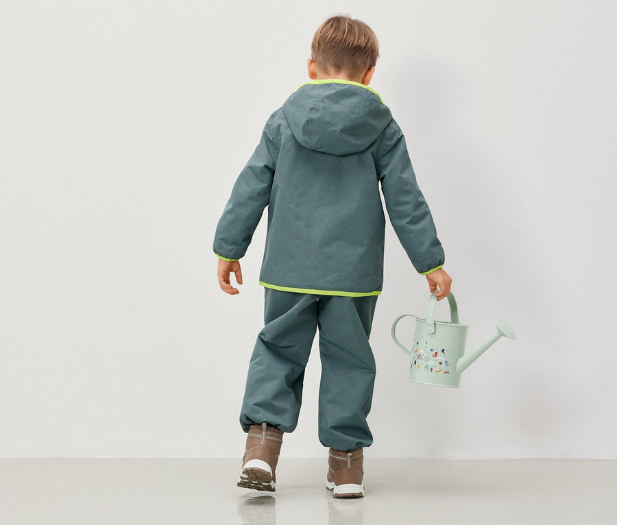 Chlapec v bundě a kalhotách s kapucí drží konev.