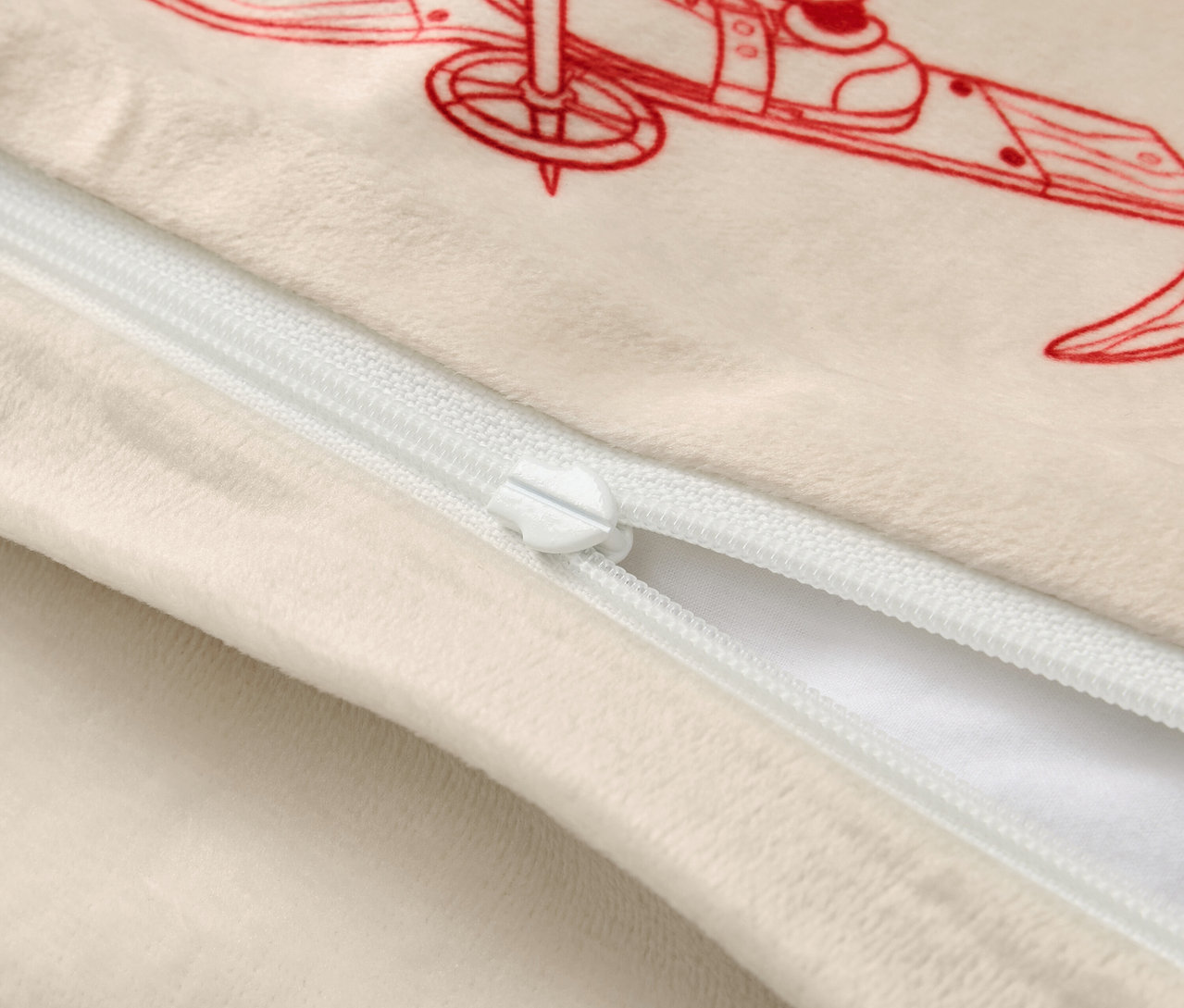 Béžový povlak na polštář s červeným obrázkem lyžaře a bílým zipem.