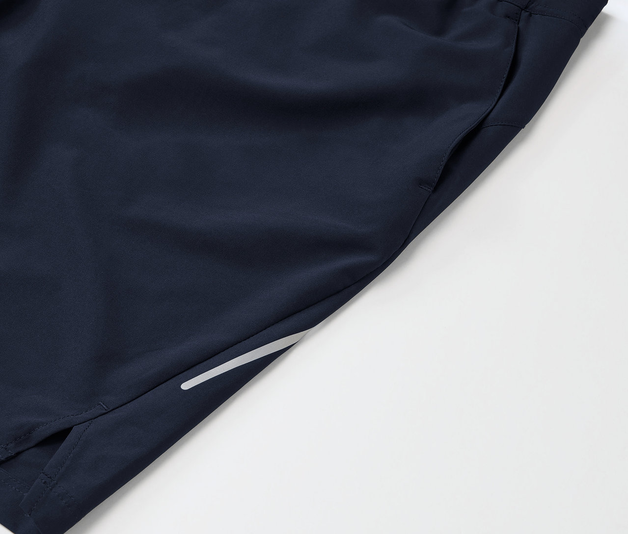 Detail tmavě modrých sportovních šortek s kapsou a reflexním prvkem na nohavici.