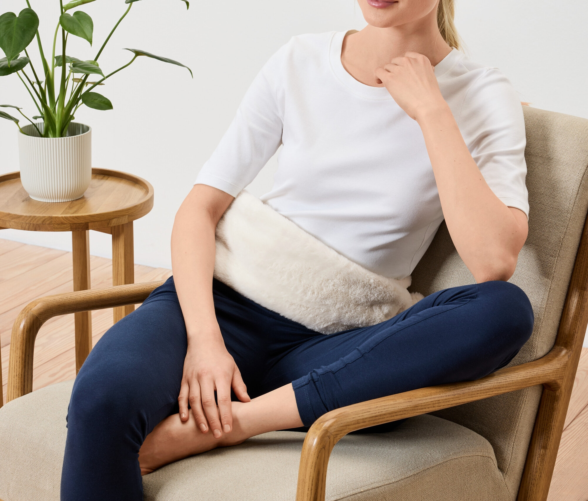 Žena sedí v křesle s hřejivým polštářkem na břiše.