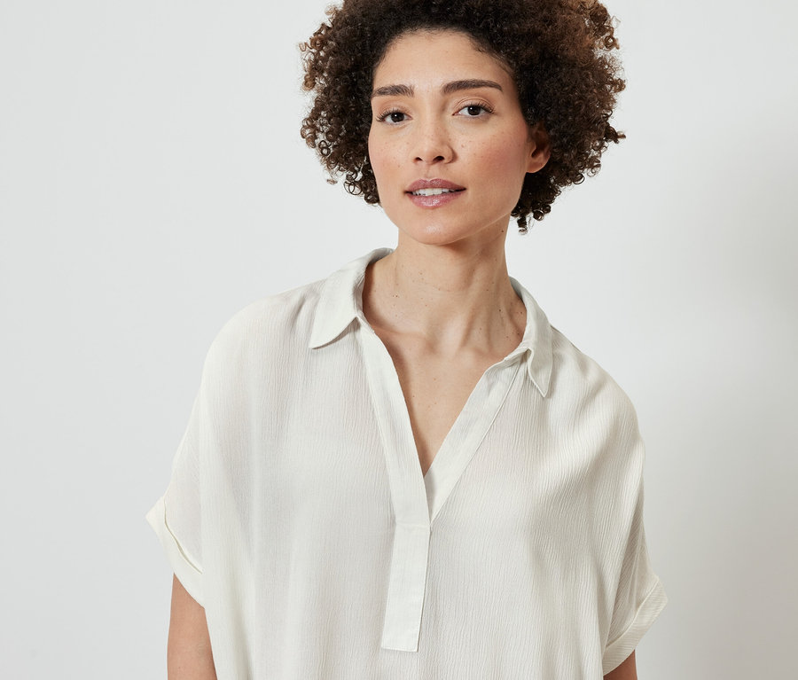 Portrét ženy s hnědými kudrnatými vlasy v krémově bílé halence.