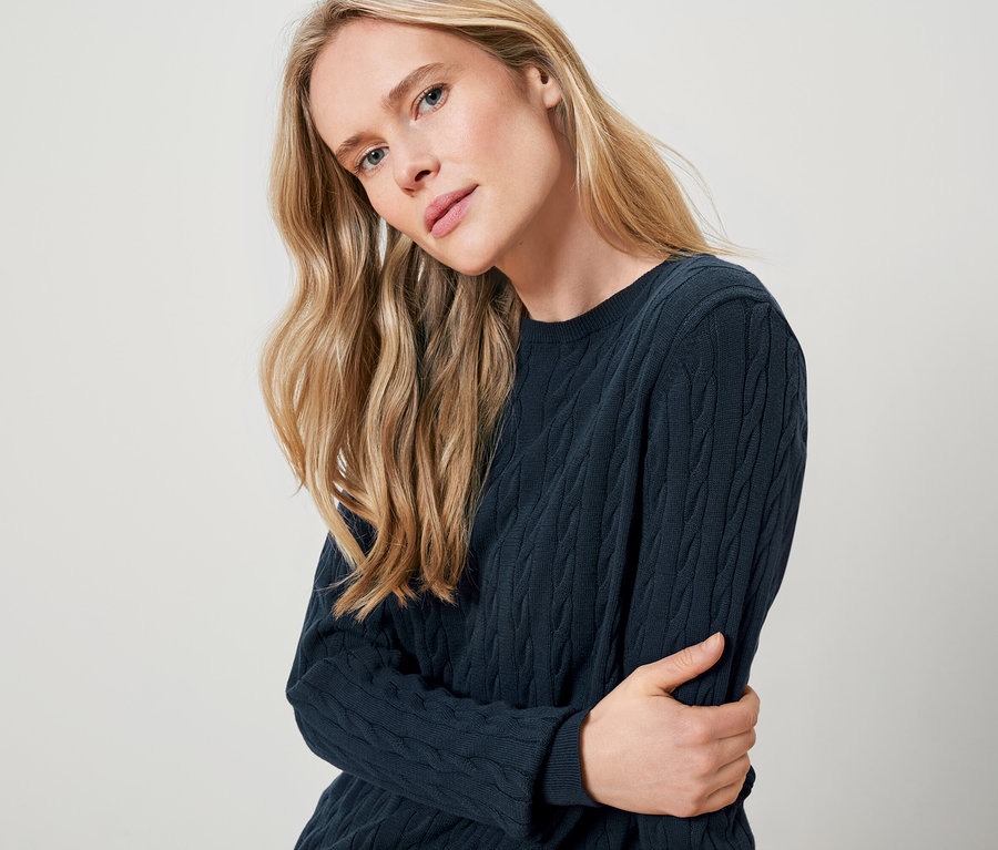 Blondýna má na sobě tmavě modrý pletený svetr.