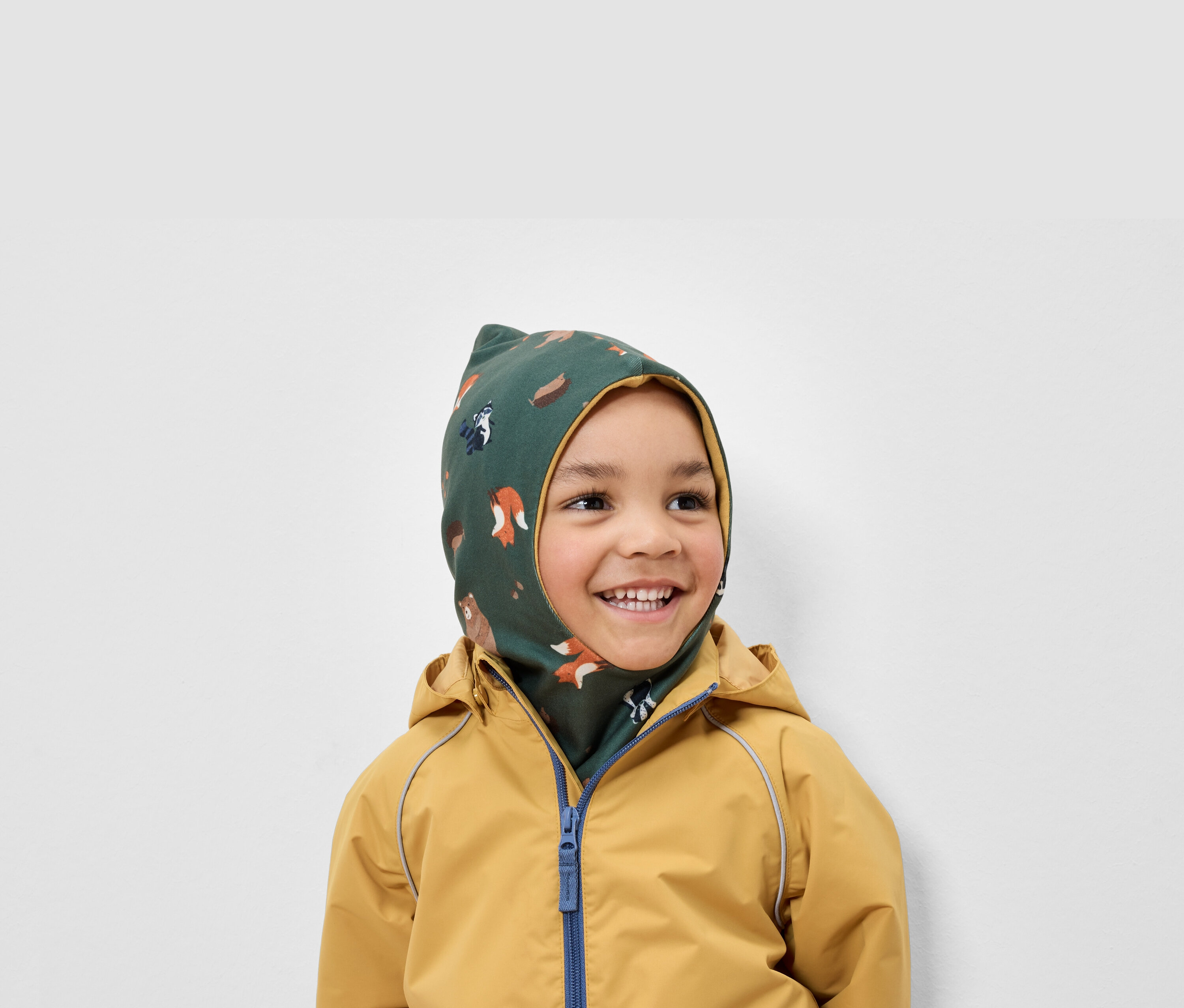 Usmívající se chlapec má na sobě zelenou kuklu s potiskem zvířat a žlutou bundu.