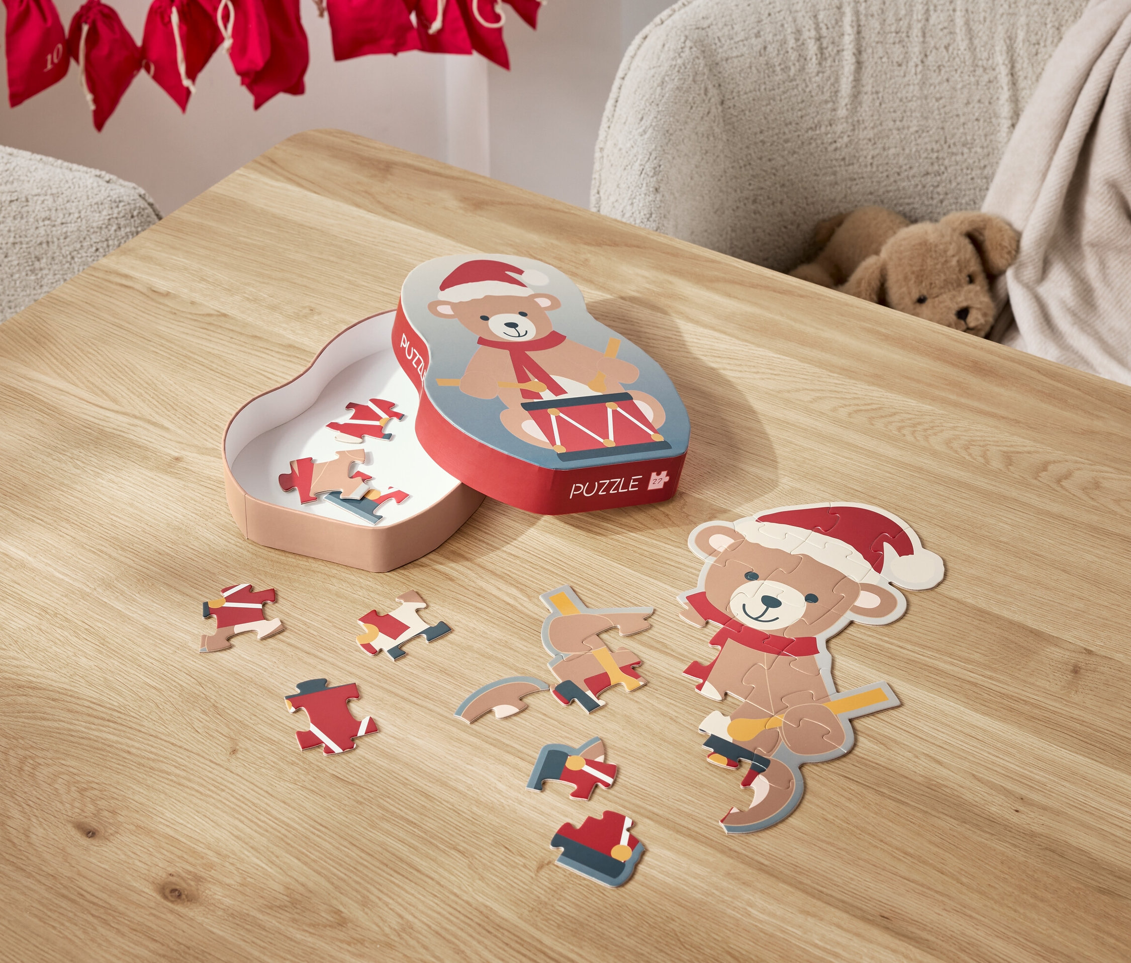 Na stole leží rozložené puzzle s motivem medvídka v santovské čepici a jeho krabička.