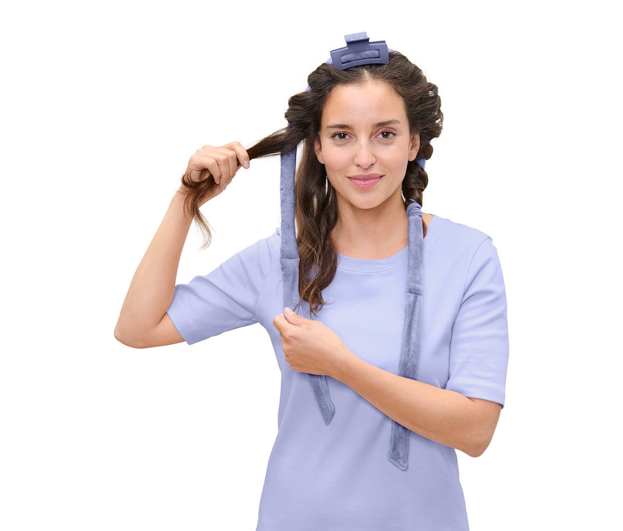 Žena si natáčí vlasy pomocí modré natáčky na vlasy.