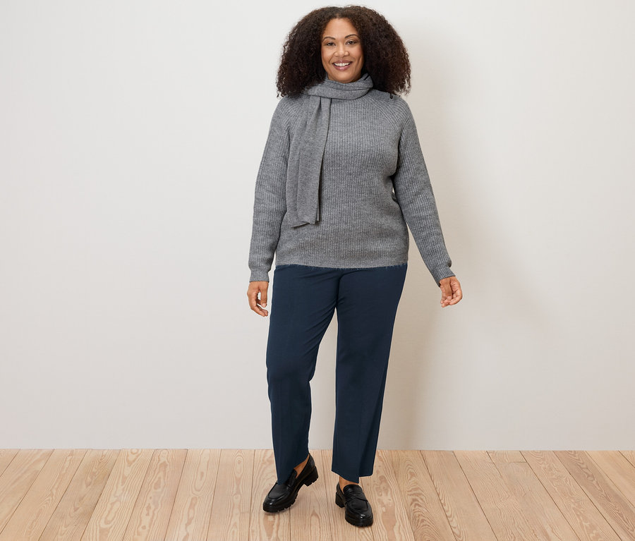 Žena nosí šedý svetr a tmavě modré pohodlné žerzejové kalhoty.