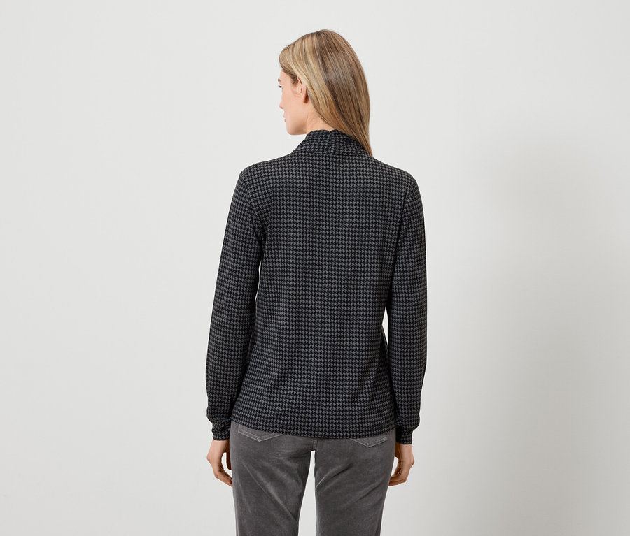 Zezadu žena v šedočerném topu s dlouhým rukávem a šedých kalhotách.