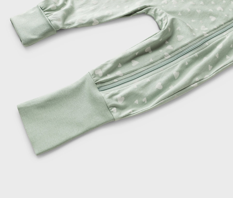 Detailní záběr světle zeleného dětského overalu s bílým vzorem srdce a zipem.