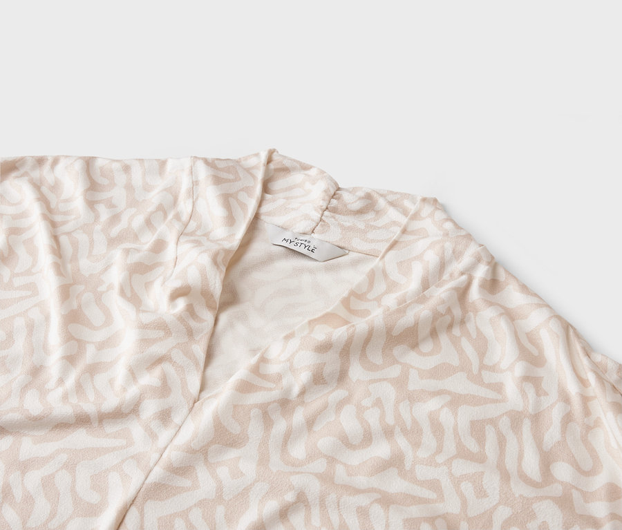 Detailní záběr světlého kabátu s abstraktním vzorem a štítkem 'MY STYLE'.