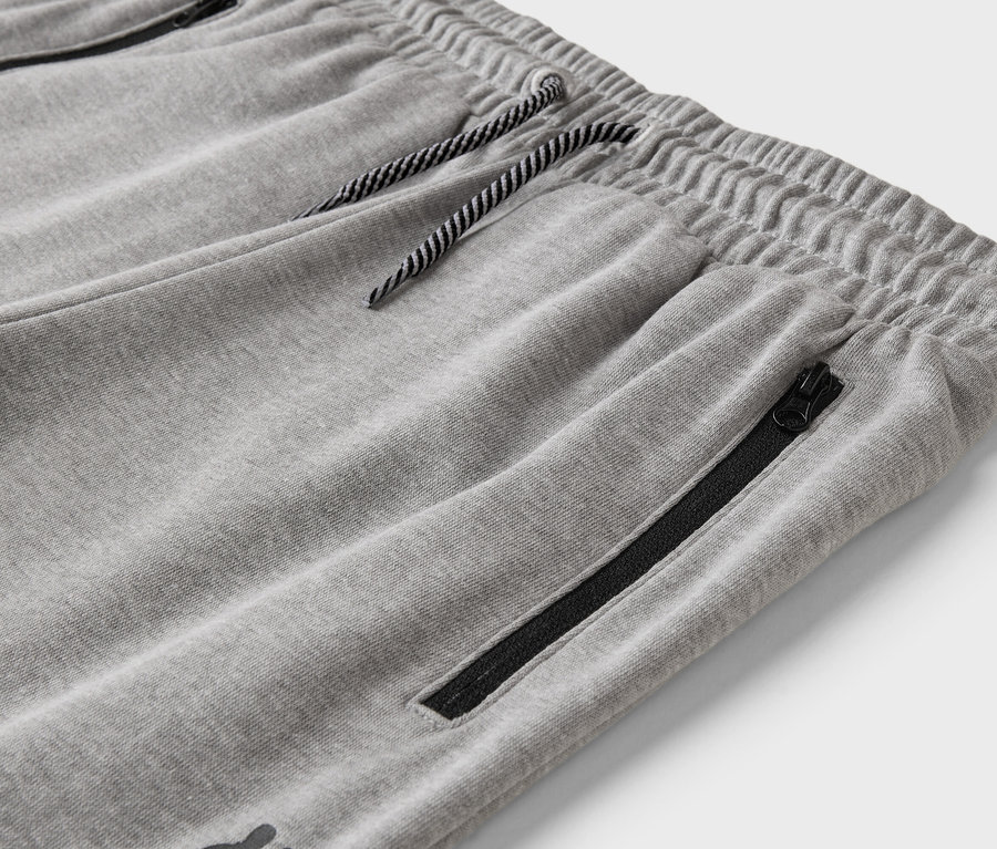 Detailní záběr šedých tepláků se stahovací šňůrkou a kapsou na zip.
