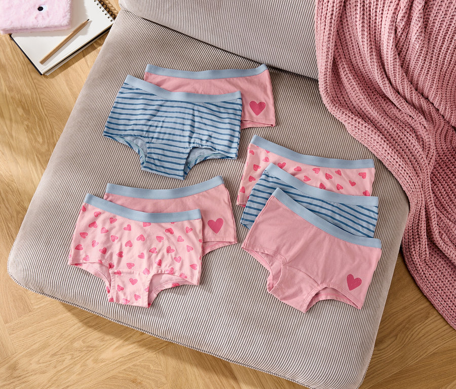 Na pruhovaném polštáři leží šest dívčích kalhotek v růžové a modré barvě.