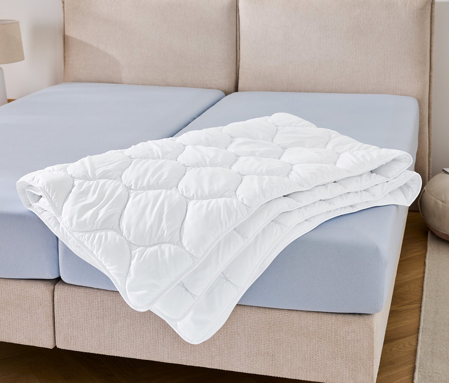 Na modrém prostěradle leží složená přikrývka odolná proti varu v nadměrné velikosti.