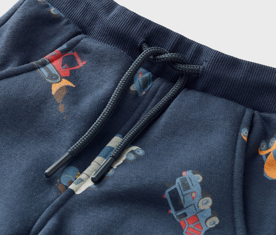 Detailní záběr na tmavě modré tepláky se stahovací šňůrkou a motivem stavebních strojů.